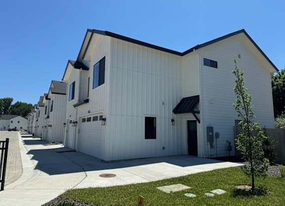 A white building with a black roof and a tree in front.
