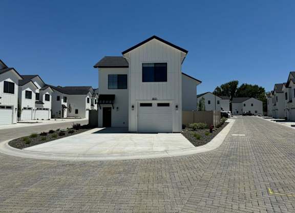 A white house with a black roof is surrounded by other similar houses.