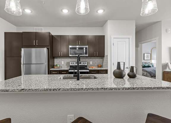 A kitchen with a granite countertop and dark brown cabinets.
