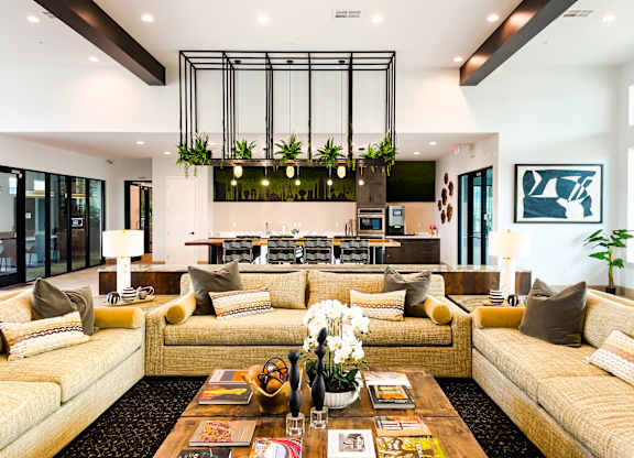 A modern living room with a large yellow sofa and a coffee table with magazines and a vase of flowers.