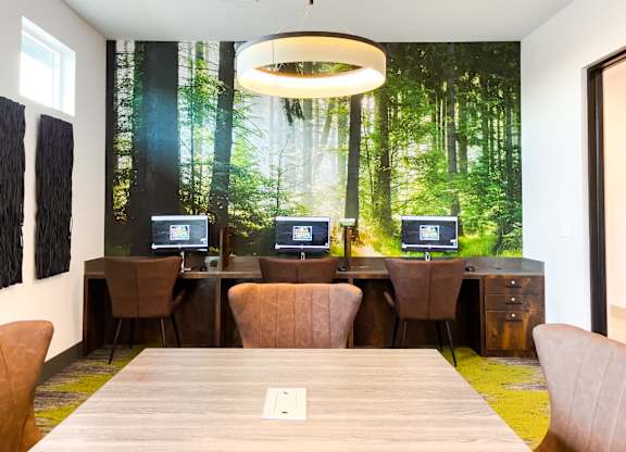 A conference room with a forest mural on the wall and four computers on desks.