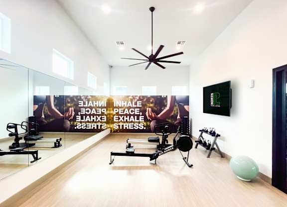 A gym room with exercise equipment and a wall mural promoting inhalation, exhalation, peace, and stress relief.
