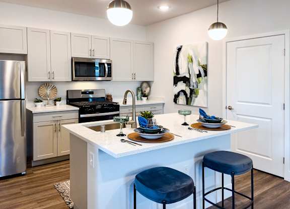 A modern kitchen with a white island and blue stools.