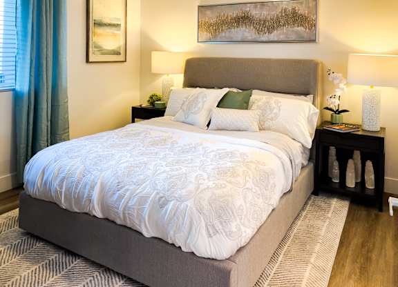 A bed with a white comforter and a grey headboard is in the image.