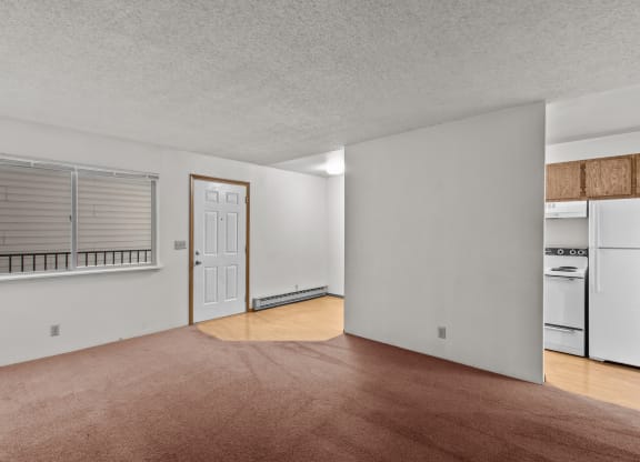 the living room and kitchen of an apartment with white appliances and wood flooring