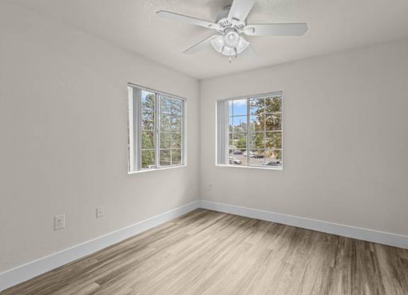 A room with a ceiling fan and two windows.