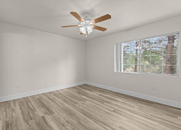 A room with a ceiling fan and a window with a view of trees.