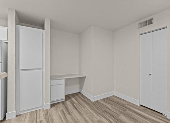 A white refrigerator is in a room with a wooden floor and white walls.