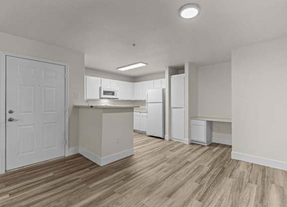A kitchen with white appliances and a wooden floor.