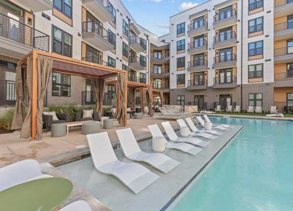 A large swimming pool with white chairs and a wooden pergola.