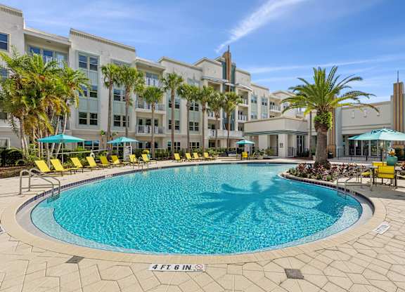 A large swimming pool surrounded by yellow chairs and palm trees.