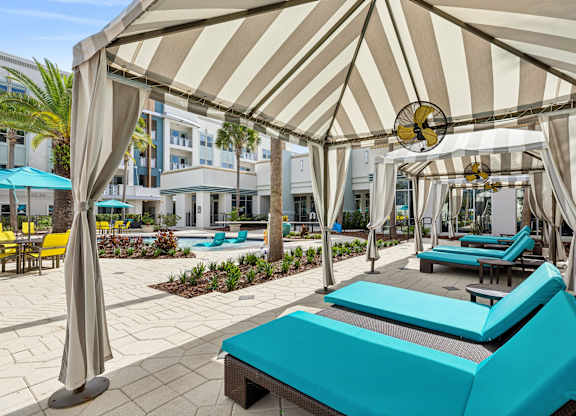 A sunny day at the pool with a striped umbrella providing shade.