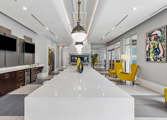 A long white table is in the middle of a room with yellow chairs on the side.