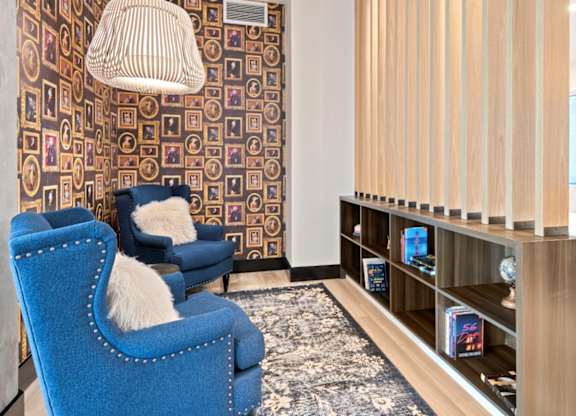 A blue chair with a white furry pillow is in front of a wall with a pattern of squares and rectangles.
