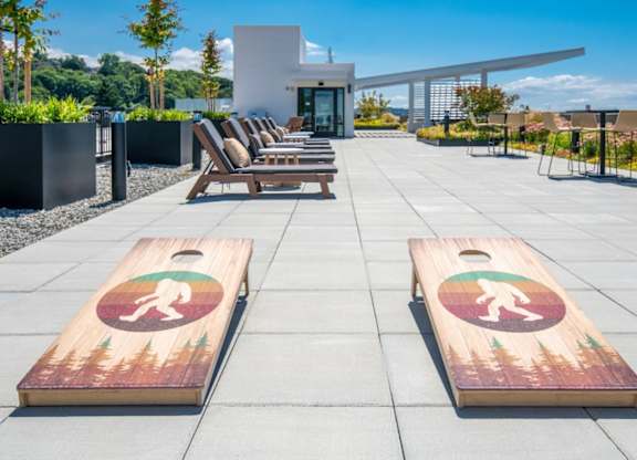A wooden cornhole game set on a patio with a modern house in the background.