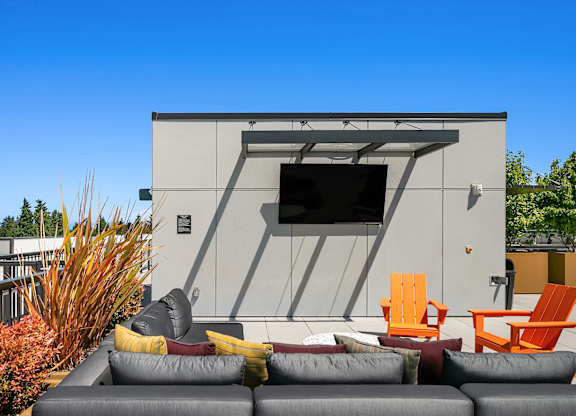 A modern outdoor seating area with a grey couch, orange chairs, and a grey sofa.