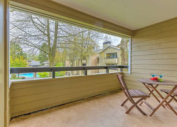 A balcony with a table and chairs overlooking a pool and trees.