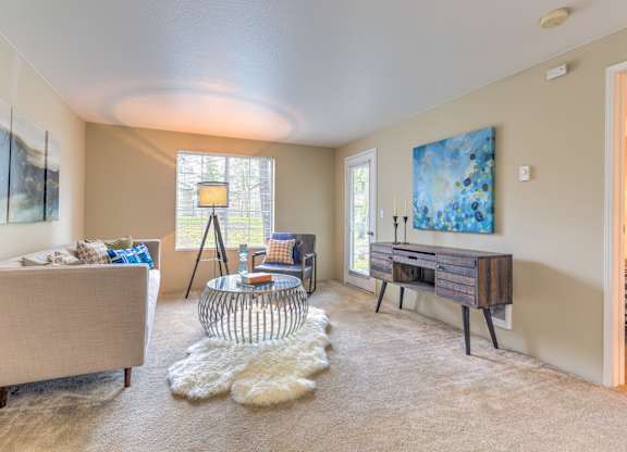 A living room with a beige couch, a glass table, and a painting on the wall.