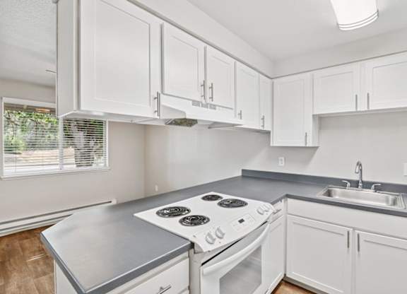 A white kitchen with a stove top oven and a sink.