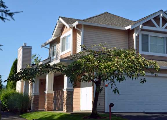 A house with a white garage door and a tree in front.