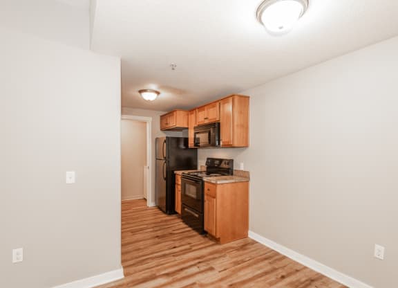 a kitchen with wood flooring and wooden cabinets and a black refrigerator