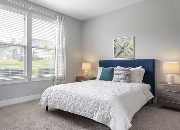 A bedroom with a large bed, two lamps, and a painting on the wall.
