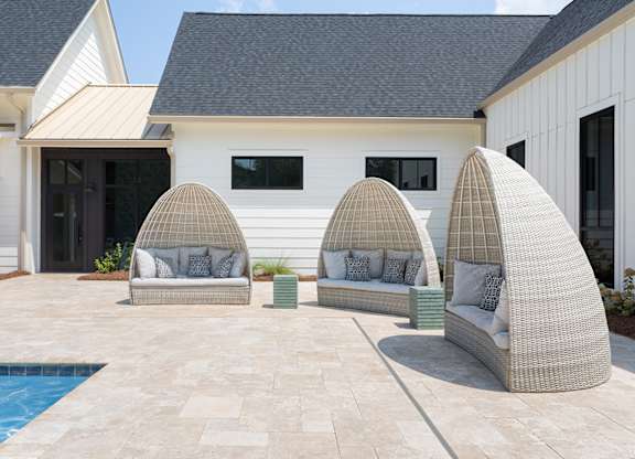A white house with a pool and three wicker chairs.