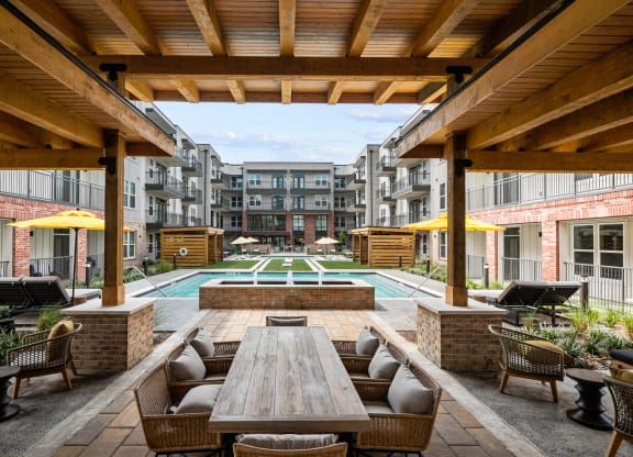 a patio with a wooden table and chairs and a pool in the background