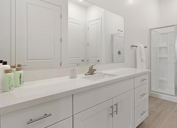 A white bathroom with a sink, mirror, and shower.