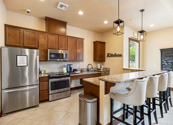 A kitchen with a refrigerator, microwave, oven, and bar stools.