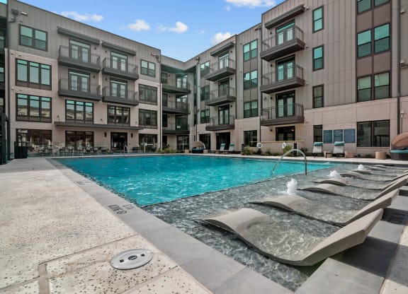 a swimming pool with chaise lounge chairs next to an apartment building