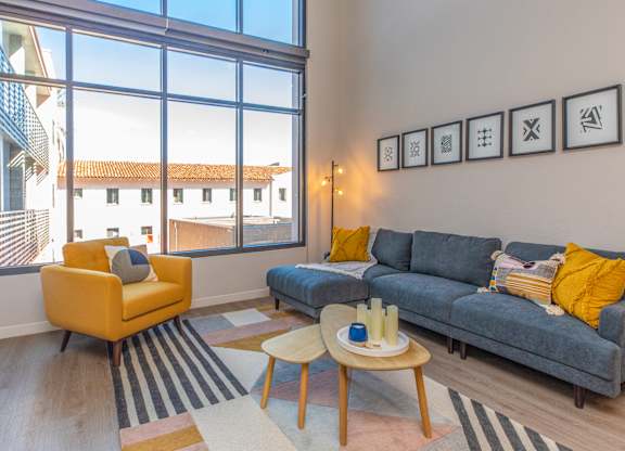A living room with a yellow chair, grey couch, and a table with candles on it.