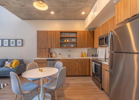 A modern kitchen with a stainless steel refrigerator, wooden cabinets, and a dining table with four chairs.