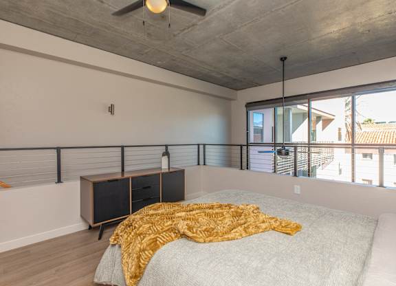 A bedroom with a bed, a ceiling fan, and a window with a view of the outside.