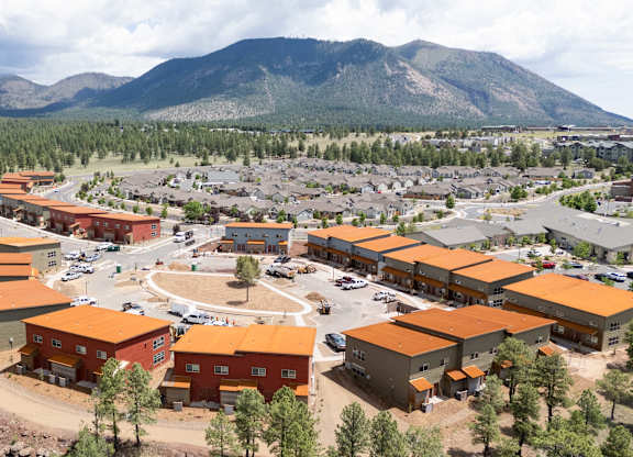 A large building complex with orange roofs is surrounded by a parking lot and trees.