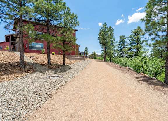 A red building is situated on a dirt road with trees on either side.
