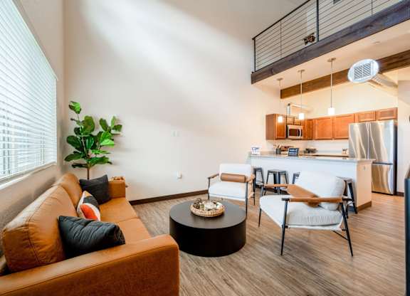A living room with a brown couch, a coffee table, and a dining area in the background.