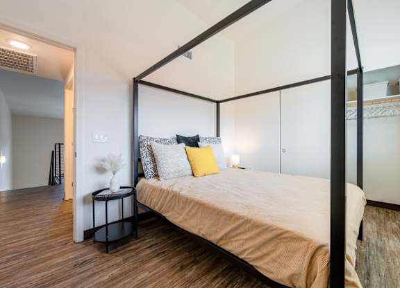 A bedroom with a four-poster bed and a nightstand with a vase of flowers on it.