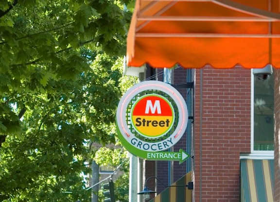 A street sign for M Street Grocery entrance is hanging from a pole.