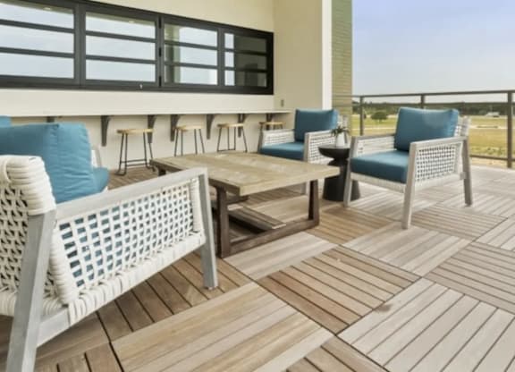 A white wicker chair is on a wooden deck with a table and other chairs.