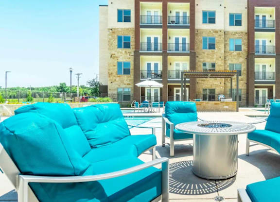 A patio with blue chairs and a table in front of a building.