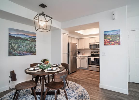 a dining area with a small table and chairs and a kitchen in the background