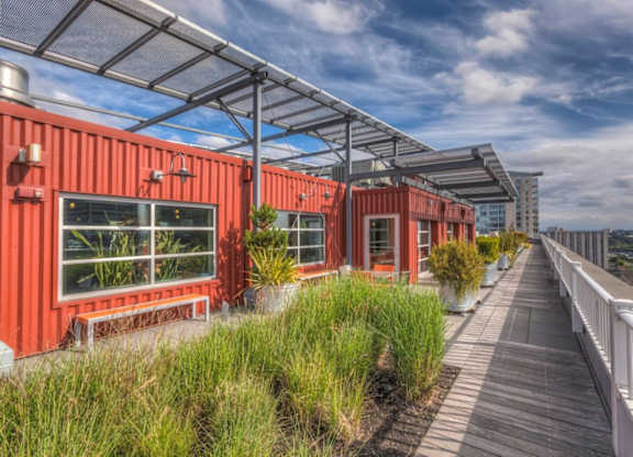 A series of red shipping containers are lined up on a wooden walkway with a metal roof above.