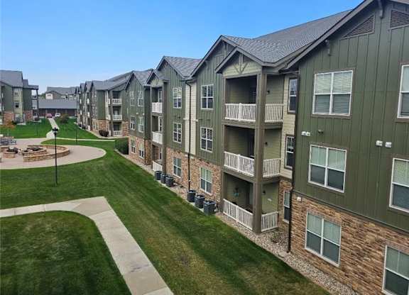 Apartment complex with green and brown buildings and a grassy area in front.