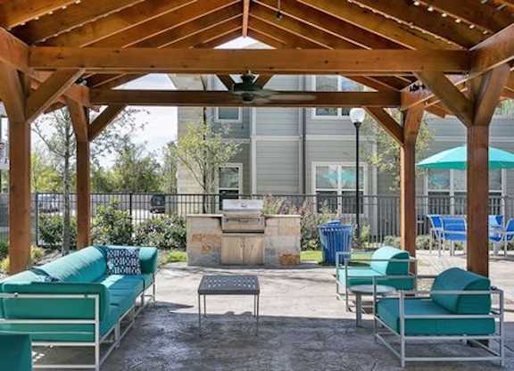 A wooden pergola with green couches and a fireplace in the middle.