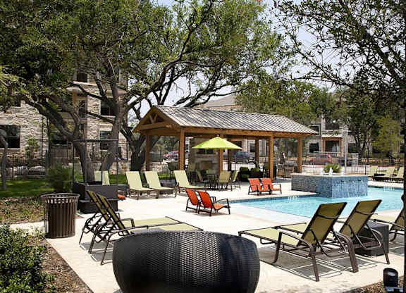 A pool area with a gazebo and lounge chairs.