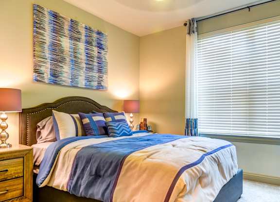 A bedroom with a bed, pillows, and a window with blinds.
