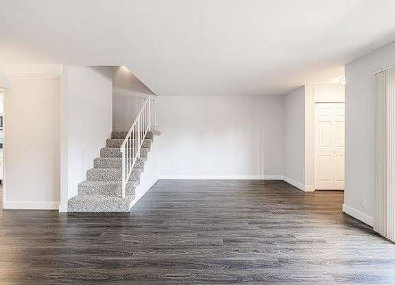 A spacious room with a staircase and wooden flooring.