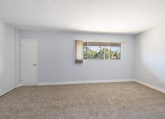 A room with a door and a window with a view of trees outside.
