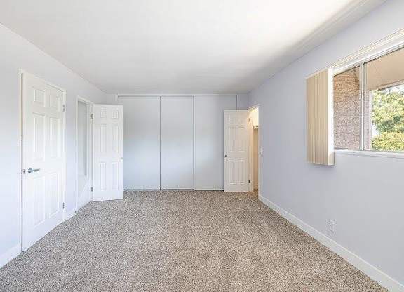 A room with white walls and a carpeted floor with a window on the right side.